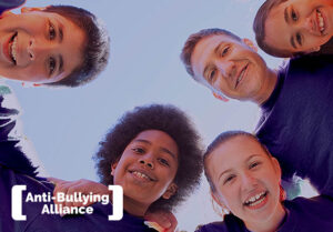 An image of a kids and one adult huddling and smiling over the camera with the Anti-Bullying Alliance logo in the bottom lefthand corner