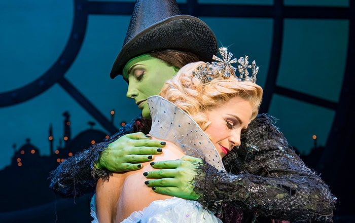 A Wicked London production image. Glinda leans her head on Elphaba's shoulder as they hug