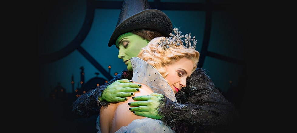 Glinda leans her head on Elphaba's shoulder as they hug