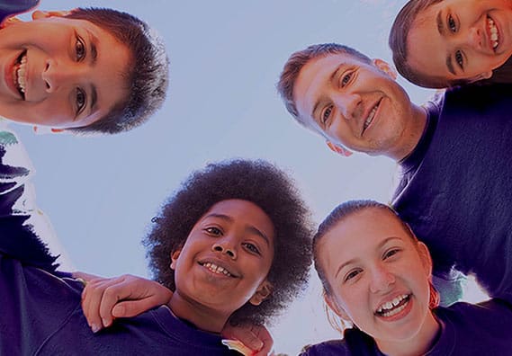 An image of a kids and one adult huddling and smiling over the camera