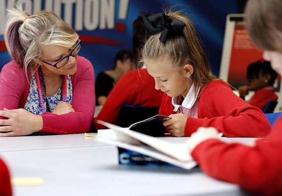 A teacher looking on as a young student in a school uniform reads