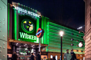 An image of the Apollo Victoria Theatre at night, showing the Wicked logo