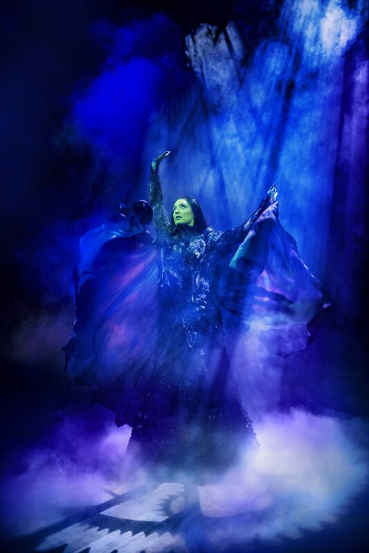 Elphaba with arms raised in the end surrounded by blue smoke