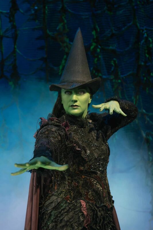 Elphaba with hands up casting a spell surrounded by smoke