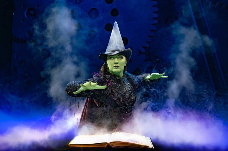 Elphaba with hands over spell book surrounded by smoke