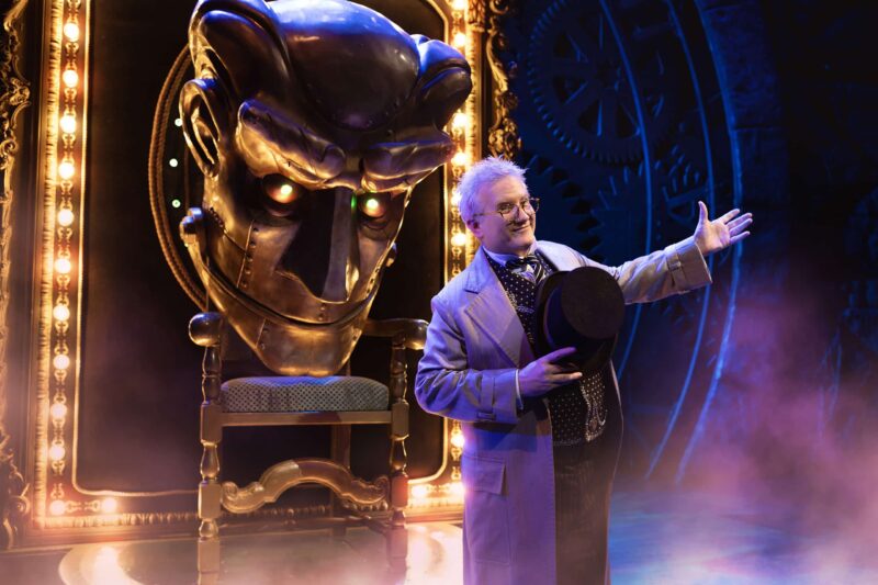 The Wizard in front of gold illuminated Oz head