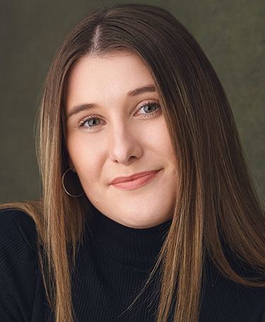Woman with straight, light brown hair wearing a black turtleneck and a hoop earring, smiling softly against a neutral, textured background.